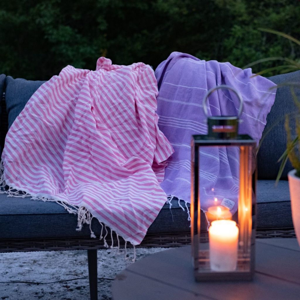 Hamam-pyyhkeet puutahratuolilla pimenevässä illassa ja lyhty jossa palaa kynttilä