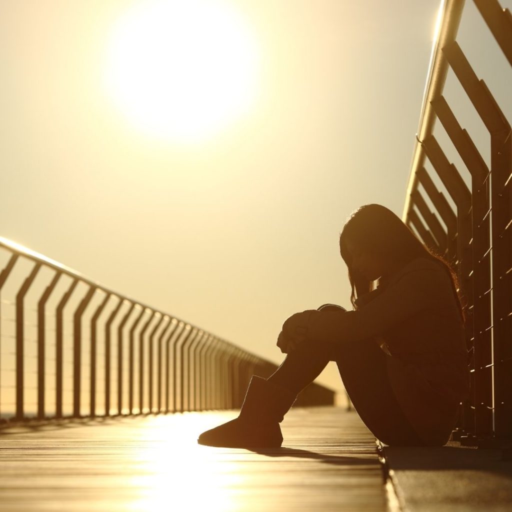 Nuori istuu sillalla masentuneena auringonlasku on taustalla