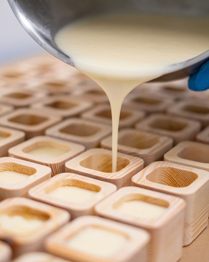 Sulatettua sheavoidetta kaadetaan käsin ekologiseen puiseen voidepakkaukseen.