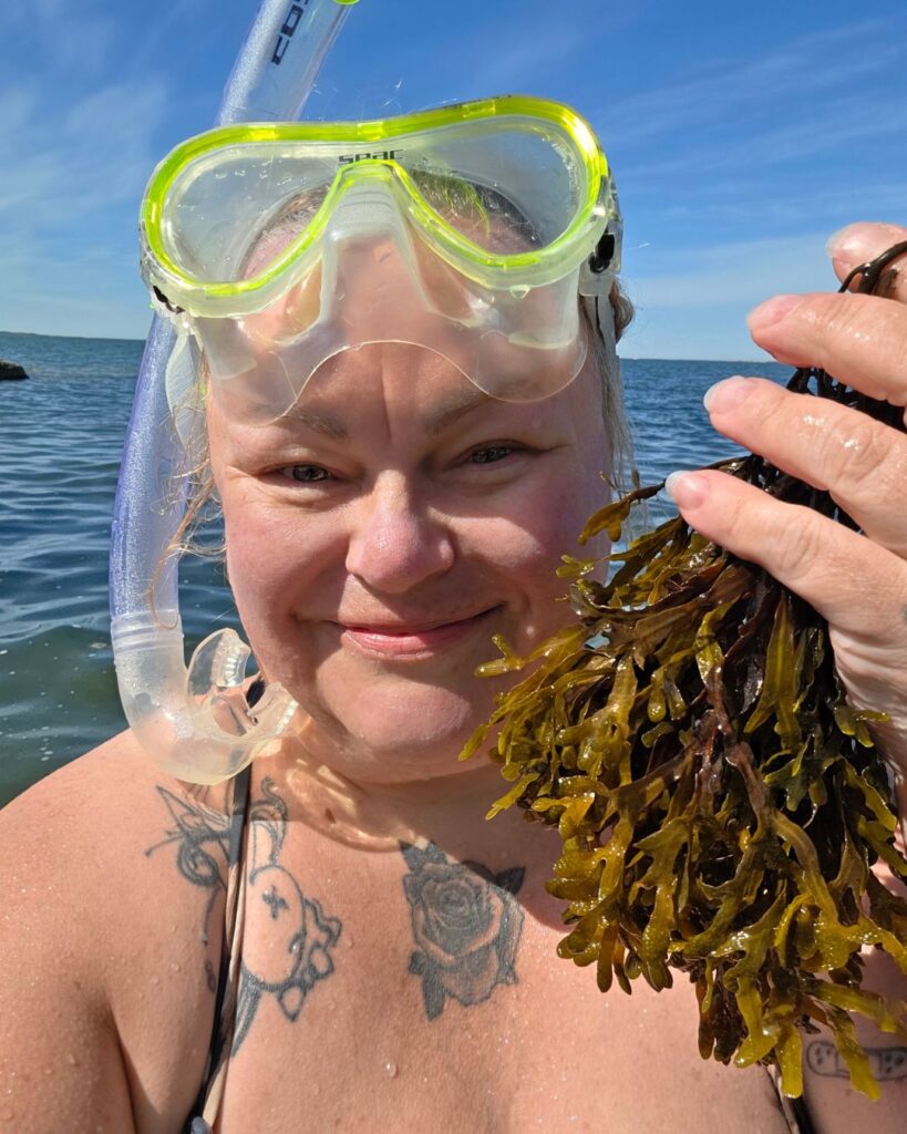 Johanna seisoo rantavedessä snorkkelit ja sukelluslasit otsalla kädessään tuoretta myrskyn irrottamaa rakkohaurua